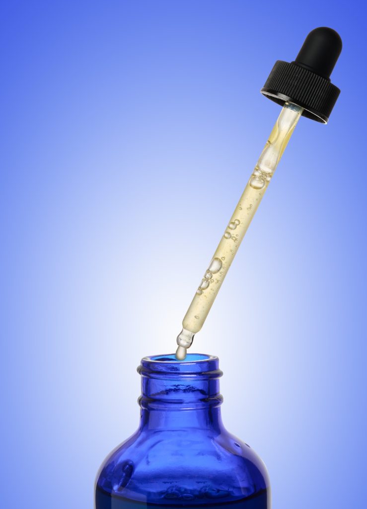 A glass blue bottle with a dropper on a blue background, a container for cosmetic products.